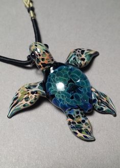 a glass turtle necklace is shown on a black cord with an animal print design and multicolored spots