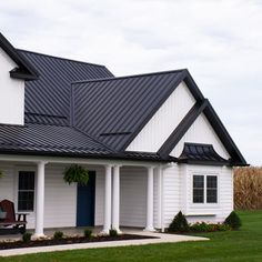 a white house with black shingles and a blue door on the front porch is surrounded by green grass