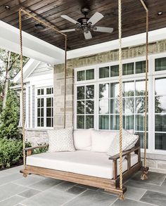 a porch swing bed with white cushions on it and a ceiling fan in the background