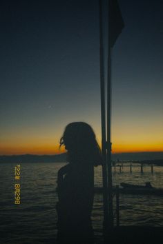 a woman standing next to the ocean at sunset