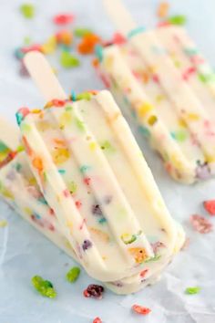 three popsicles with white frosting and multicolored candy toppings on them