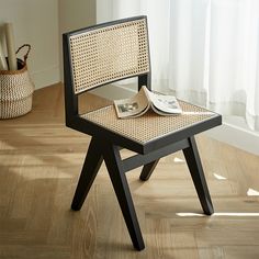 a chair with a magazine on it sitting in front of a window next to a basket