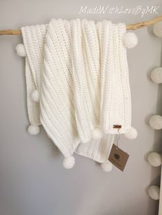 a white knitted blanket hanging on a clothes line with pom - poms