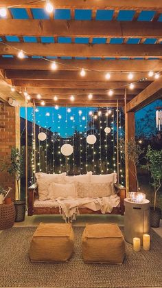 an outdoor living area with lights and pillows on the couches, in front of a pergolated patio