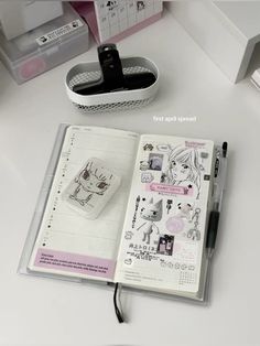 an open planner book sitting on top of a white desk next to a cup and pen