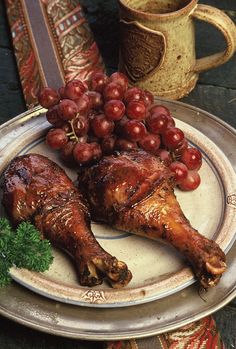 two pieces of chicken on a plate with grapes next to a coffee cup and saucer