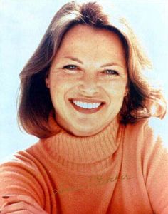 a woman smiling and wearing an orange sweater