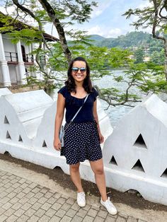 a woman standing in front of a white fence with trees and water in the background