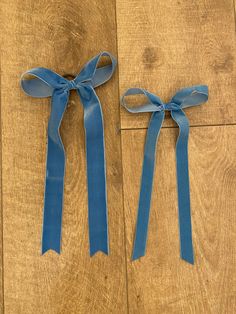 two blue ribbons tied to each other on a wooden floor next to another pair of scissors