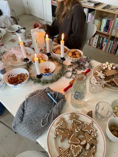 a woman sitting at a table with cookies and other food on it in front of her