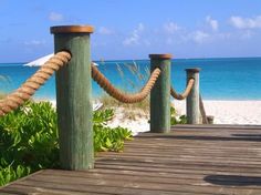 a wooden dock leading to the beach with blue water and white sand in the background