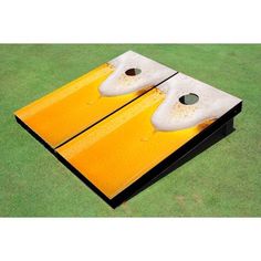 a yellow and black cornhole board with two holes in the middle on green grass