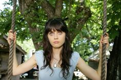 a woman is sitting on a swing with her hands in the air and looking at the camera