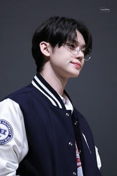 a young man wearing glasses and a baseball jacket