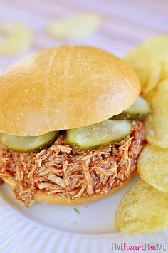 a pulled pork sandwich with pickles and potato chips