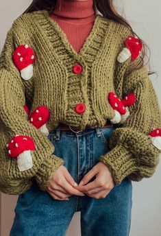 a woman wearing a green knitted sweater with red and white mushrooms on the sleeves