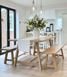 a dining room table with two benches next to it and flowers in a vase on the table