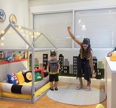 a woman and child standing in front of a bed with a batman costume on it