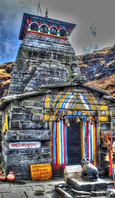 an old stone building with colorful decorations on the side and mountains in the back ground