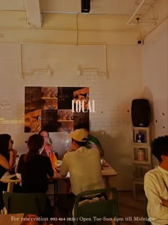 several people sitting around a table in a room with white walls and exposed ceilinging