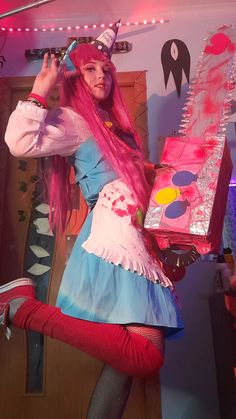 a woman with pink hair wearing a costume and holding a brush in her hand while standing next to a mirror