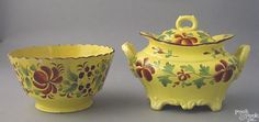 two pieces of yellow pottery with flowers and leaves painted on the sides, one is sitting next to another bowl