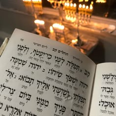 an open book with hebrew writing on it in front of lit candles and chandelier