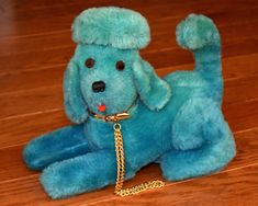 a blue stuffed dog with a gold chain around its neck sitting on the floor next to a wooden floor