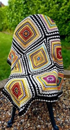 a crocheted chair sitting on top of a pile of rocks next to some bushes