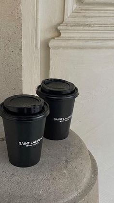 two black coffee cups sitting on top of a cement pillar next to a white door