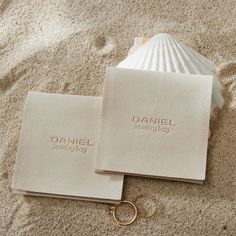 two personalized business cards laying on the sand with a gold ring in front of them