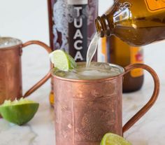 a person pours an alcoholic beverage into a copper mug with lime wedges on the rim