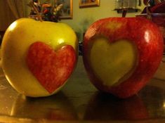 two apples with hearts cut out of them sitting on a table in front of a mirror