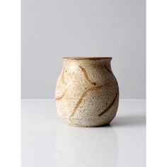 a white and brown vase sitting on top of a table next to a gray wall