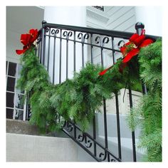 christmas wreaths on the railing of a house decorated with red bows and evergreen leaves