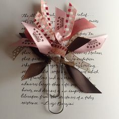 a pink and brown pinwheel with ribbon on it's side sitting on top of a piece of paper