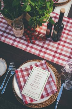 a place setting with red and white checkered table cloth, silverware, wine bottles and flowers