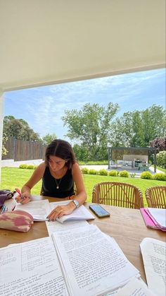 a woman sitting at a table with papers on top of it and writing in a notebook