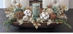 a candle is sitting on top of a wooden tray with greenery and cotton balls