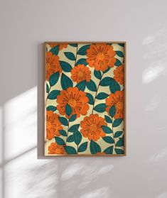 an orange and green flowered painting hanging on a white wall next to a window