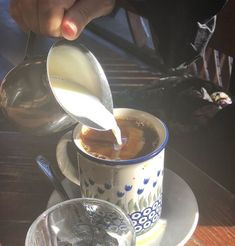 a person pouring milk into a cup on top of a saucer with spoons