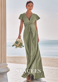 a woman in a long green dress standing on the beach with her hands in her pockets