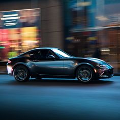 a black sports car driving down the street at night time with blurry buildings in the background