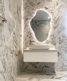 a bathroom with marble walls and flooring has a large round mirror above the sink