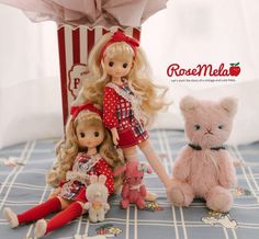 two dolls and a teddy bear sitting on a bed