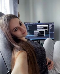 a woman sitting in front of a computer monitor with her head turned to the side