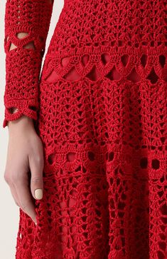 a woman wearing a red crocheted dress with holes on the sleeves and bottom