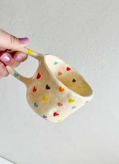 a hand holding a ceramic cup with hearts painted on the outside and inside, in front of a white wall