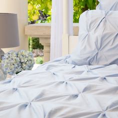 a bed with blue sheets and pillows in a bedroom next to a table with flowers on it