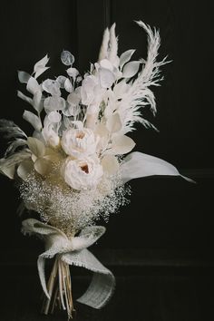 a bouquet of white flowers and feathers on a black background with some silver flakes